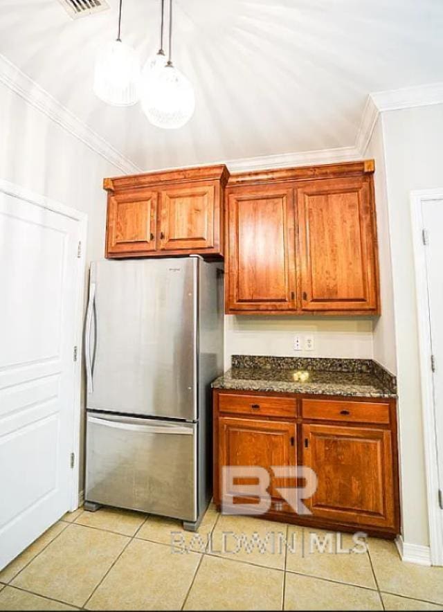 kitchen with light tile patterned floors, stainless steel fridge, dark stone countertops, and ornamental molding