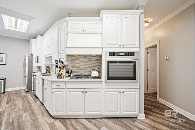 kitchen with white cabinets, sink, appliances with stainless steel finishes, light hardwood / wood-style floors, and custom range hood