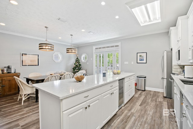 kitchen with pendant lighting, stainless steel fridge, a kitchen island, light hardwood / wood-style floors, and white cabinetry