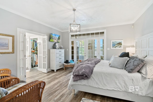 bedroom with access to exterior, french doors, crown molding, wood-type flooring, and a notable chandelier