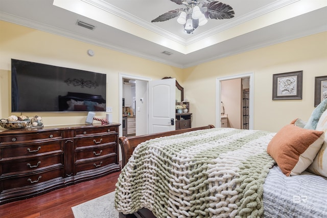 bedroom featuring ceiling fan, dark wood-type flooring, a raised ceiling, ensuite bathroom, and crown molding