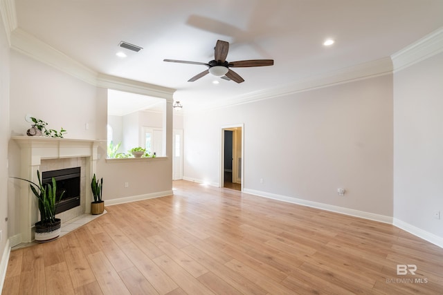 unfurnished living room with ceiling fan, a tiled fireplace, light hardwood / wood-style flooring, and ornamental molding