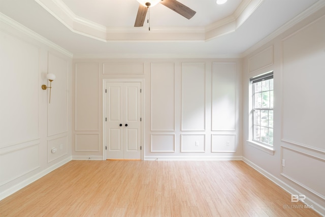 unfurnished room with light wood-type flooring, a tray ceiling, ceiling fan, and ornamental molding