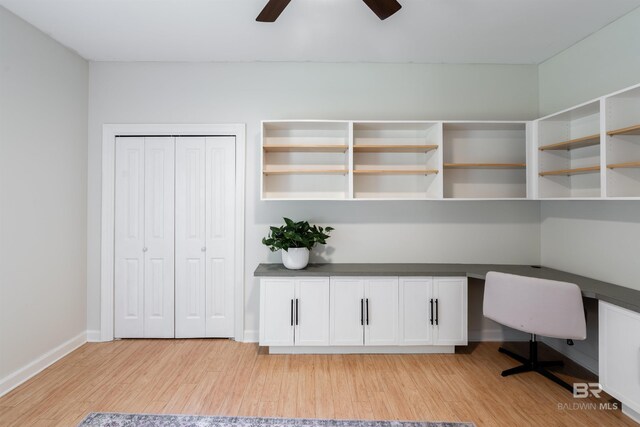 unfurnished office with ceiling fan, built in desk, and light wood-type flooring