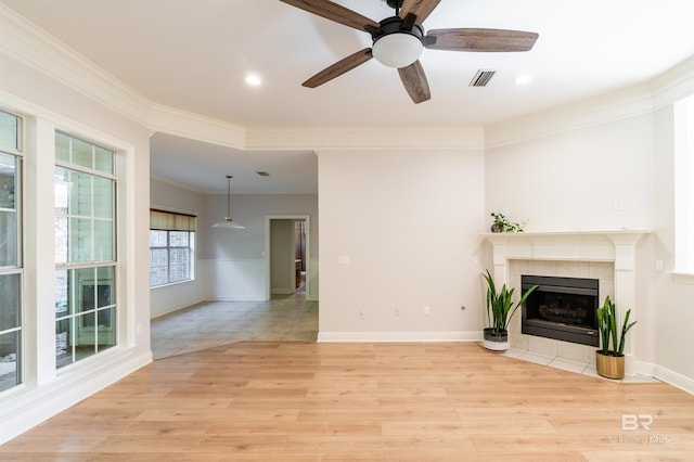 unfurnished living room featuring ceiling fan, a tiled fireplace, light hardwood / wood-style floors, and crown molding