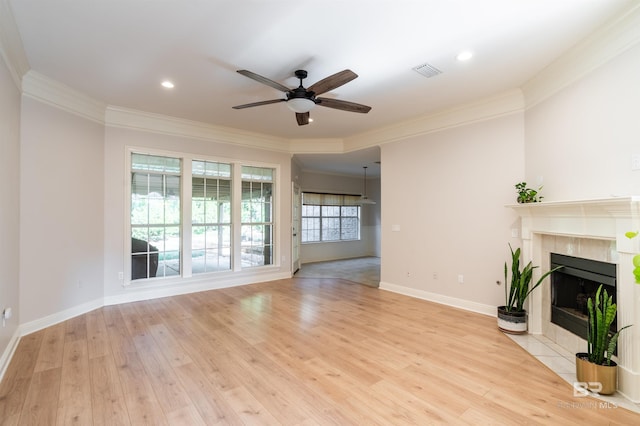 unfurnished living room with a tile fireplace, ornamental molding, ceiling fan, and light wood-type flooring