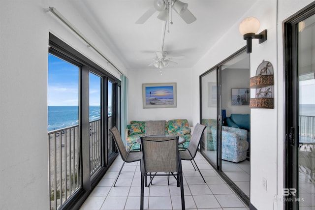 sunroom / solarium featuring ceiling fan, a water view, and a view of the beach