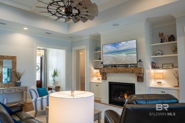 living room featuring a glass covered fireplace, a ceiling fan, ornamental molding, light wood finished floors, and a raised ceiling