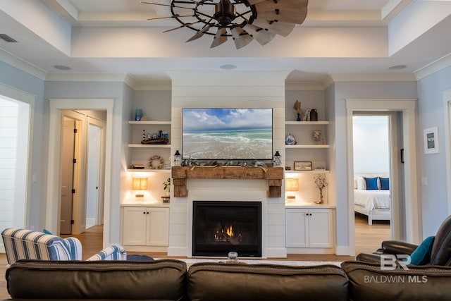 living area featuring a tray ceiling, a fireplace, wood finished floors, and crown molding