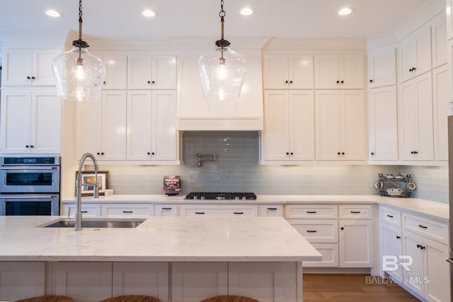 kitchen with double oven, a breakfast bar, a sink, gas stovetop, and white cabinets