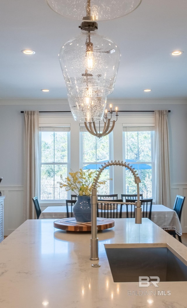 interior details featuring light stone counters, a decorative wall, wainscoting, and an inviting chandelier