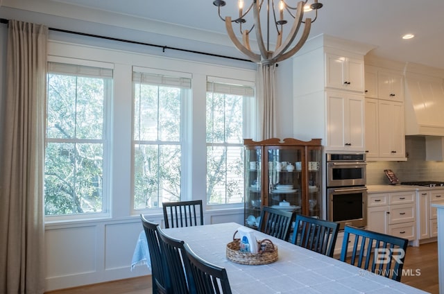 dining room featuring a chandelier, a decorative wall, wood finished floors, and a healthy amount of sunlight