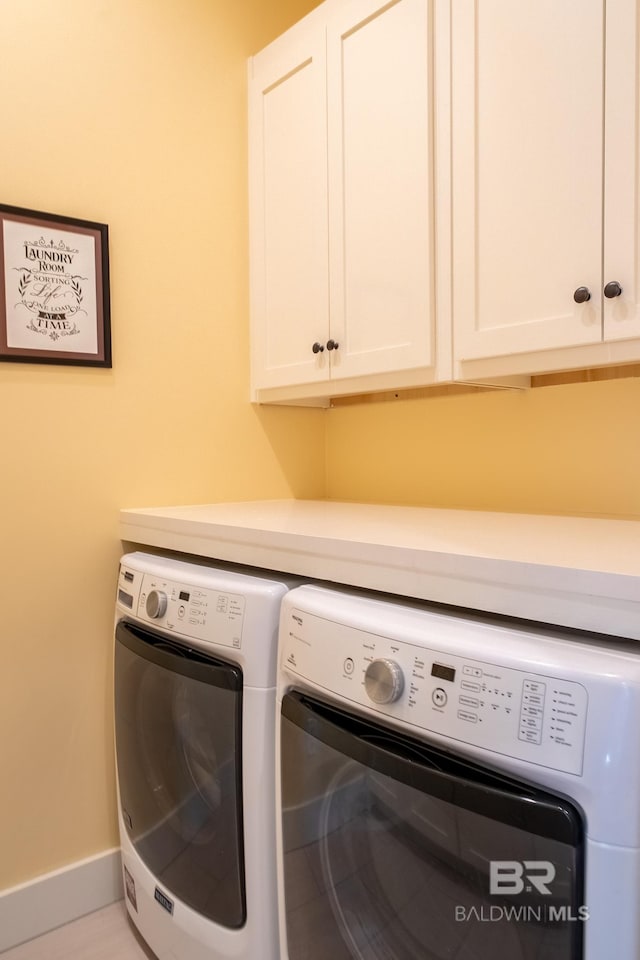 clothes washing area featuring washing machine and clothes dryer, cabinet space, and baseboards