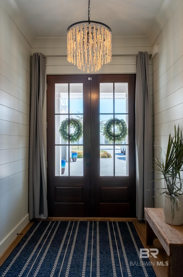 entryway with french doors, a healthy amount of sunlight, a notable chandelier, and wood walls