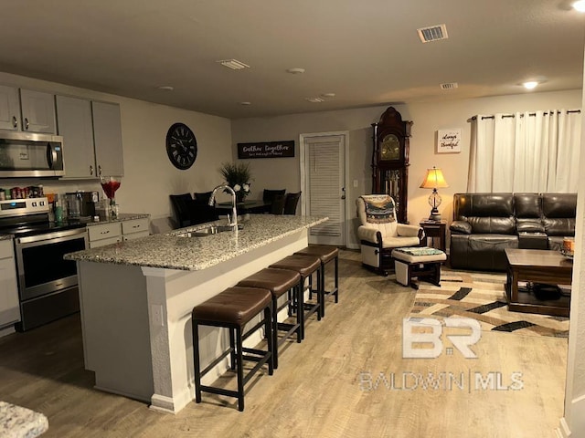 kitchen featuring a breakfast bar, stainless steel appliances, gray cabinetry, a kitchen island with sink, and a sink