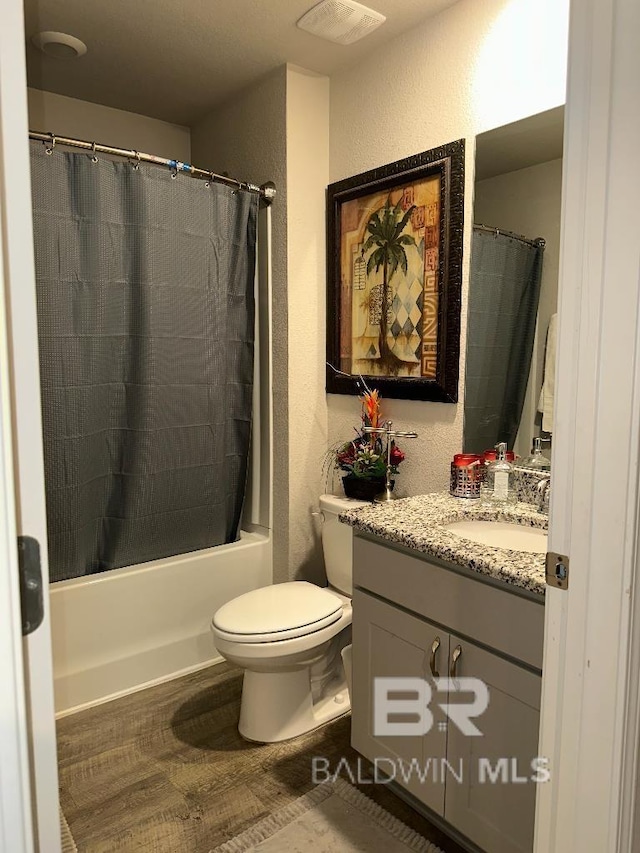 bathroom featuring visible vents, a textured wall, wood finished floors, shower / bath combination with curtain, and vanity