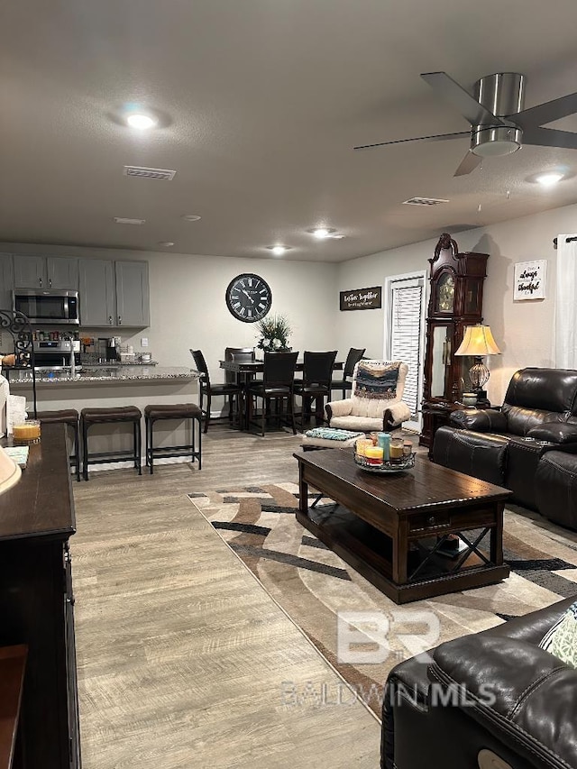 living room with ceiling fan, light wood-style flooring, and visible vents