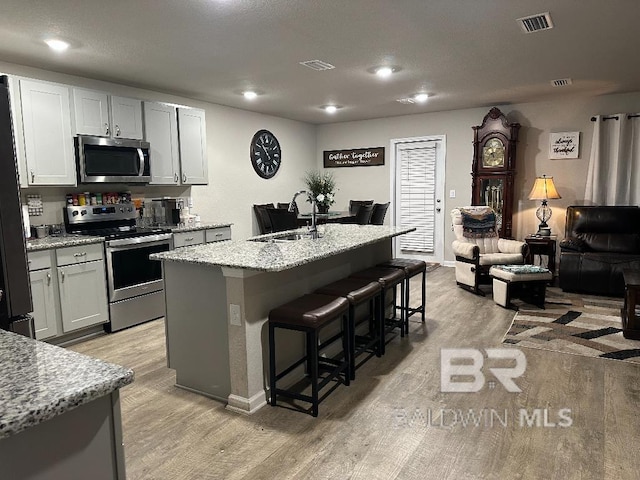 kitchen featuring visible vents, an island with sink, appliances with stainless steel finishes, light stone counters, and a sink