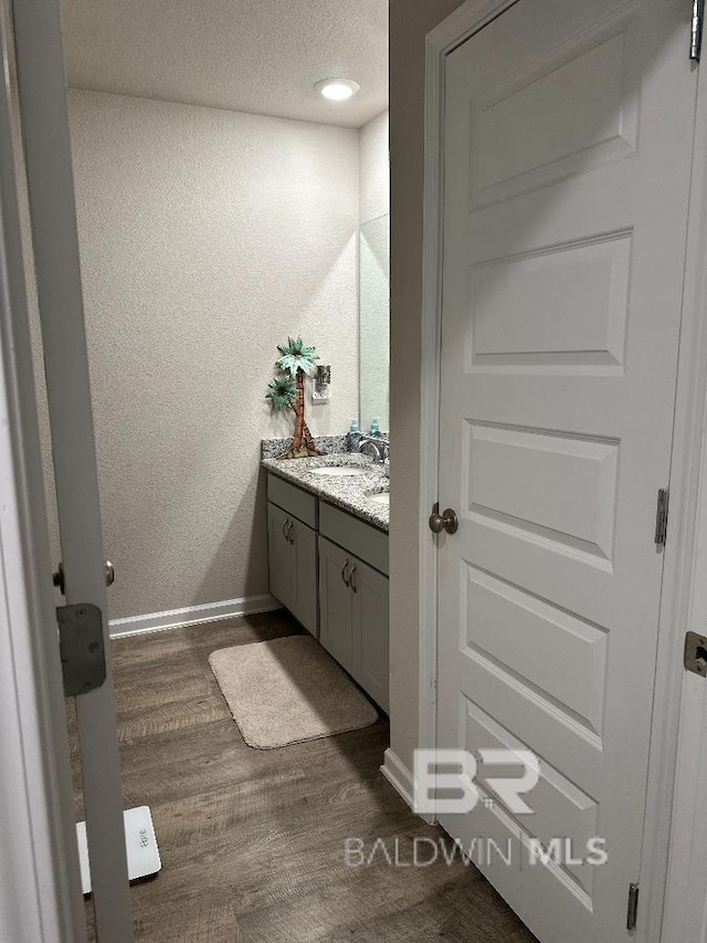 bathroom featuring baseboards, a textured wall, wood finished floors, a textured ceiling, and vanity