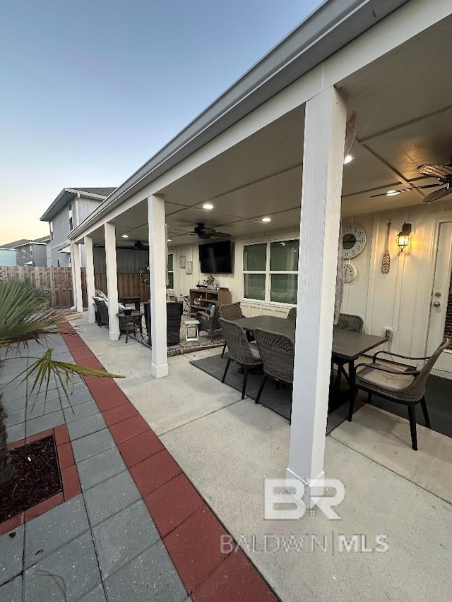 patio terrace at dusk with outdoor dining space, fence, and a ceiling fan