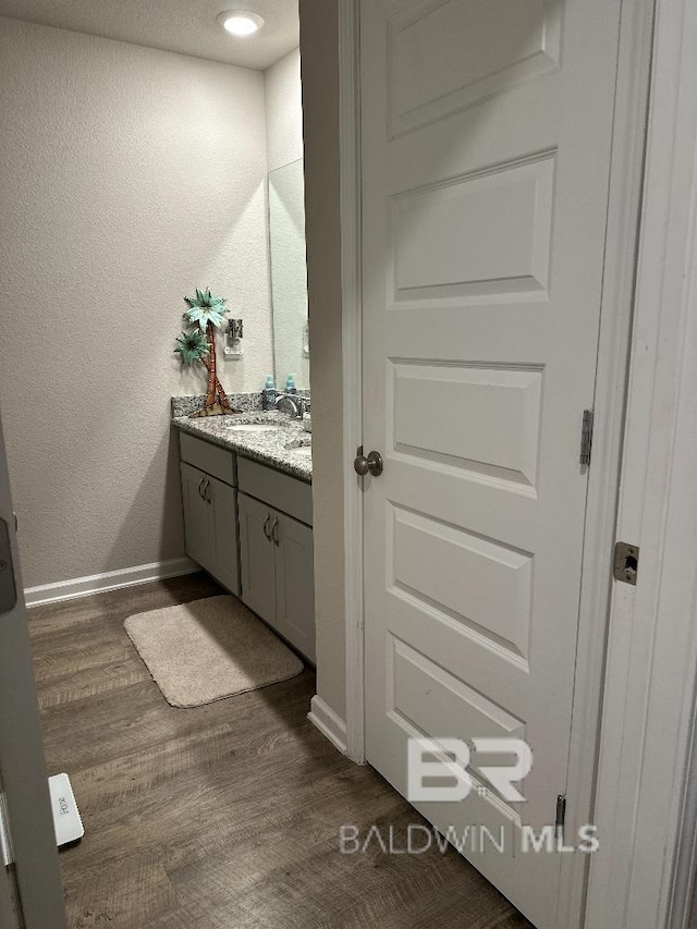 bathroom with a textured wall, vanity, baseboards, and wood finished floors