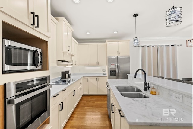 kitchen featuring light wood finished floors, pendant lighting, light stone counters, appliances with stainless steel finishes, and a sink