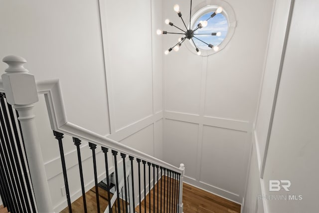 stairs with a decorative wall, an inviting chandelier, and wood finished floors