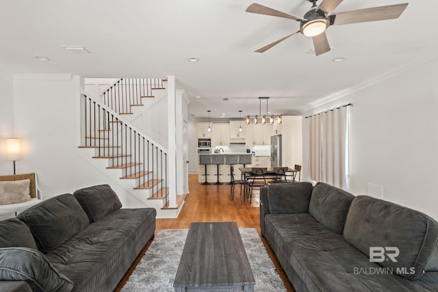 living room with light wood-style flooring, recessed lighting, stairway, crown molding, and ceiling fan