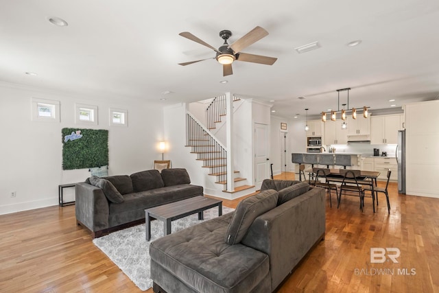 living area with recessed lighting, baseboards, light wood-style flooring, and stairs