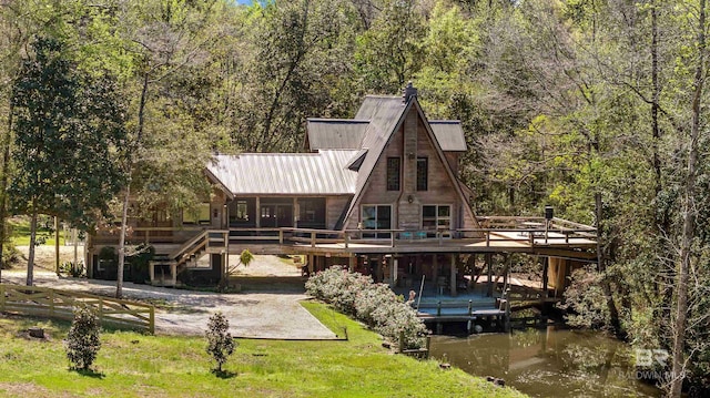 back of property featuring a deck with water view, stairs, a forest view, and a yard