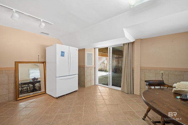 kitchen with freestanding refrigerator, wainscoting, lofted ceiling, light tile patterned floors, and tile walls