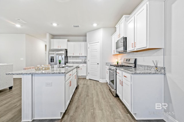 kitchen with white cabinets, stainless steel appliances, and light stone countertops