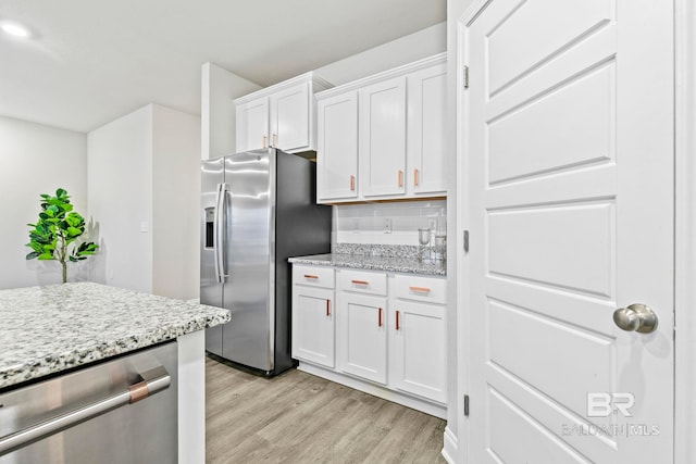 kitchen featuring light stone countertops, appliances with stainless steel finishes, backsplash, light wood-type flooring, and white cabinetry