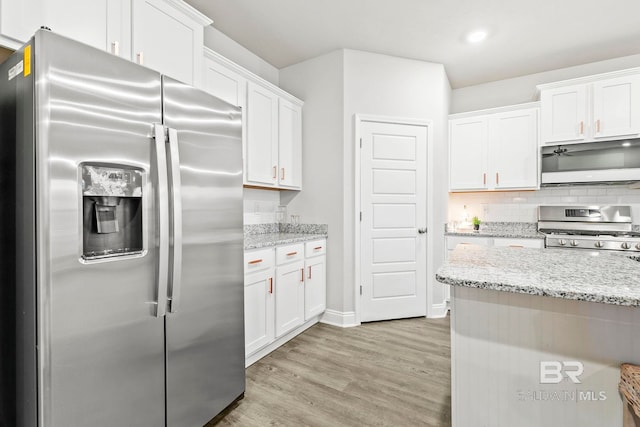 kitchen featuring white cabinetry, light stone counters, backsplash, light hardwood / wood-style floors, and appliances with stainless steel finishes