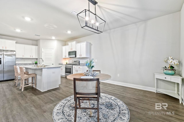 kitchen with light stone counters, stainless steel appliances, a kitchen island with sink, decorative light fixtures, and white cabinetry