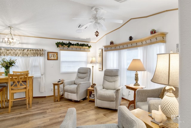 living area featuring a healthy amount of sunlight, light wood-type flooring, vaulted ceiling, and ceiling fan with notable chandelier