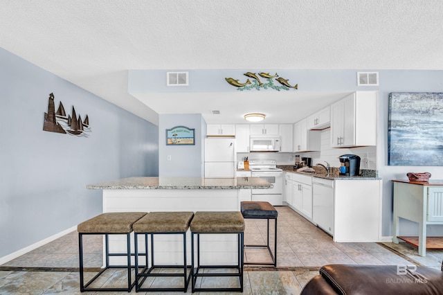 407 W Beach Blvd Unit 570, Gulf Shores, AL 36542 - kitchen with white appliances, a sink, stone counters, a breakfast bar, and white cabinetry
