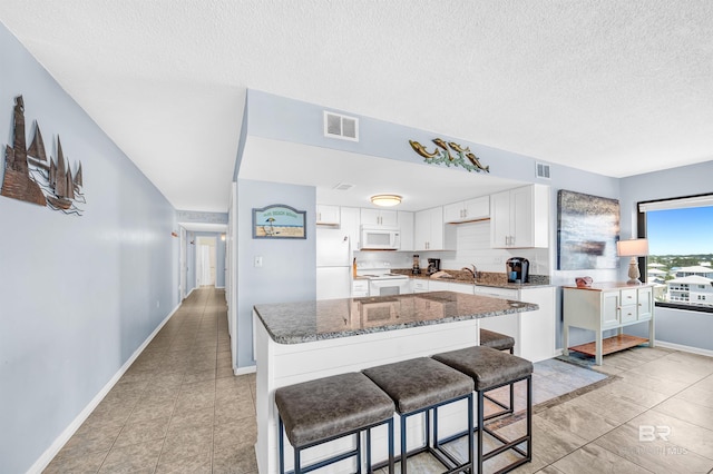 407 W Beach Blvd Unit 570, Gulf Shores, AL 36542 - kitchen with white appliances, dark stone counters, a textured ceiling, white cabinets, and a kitchen bar
