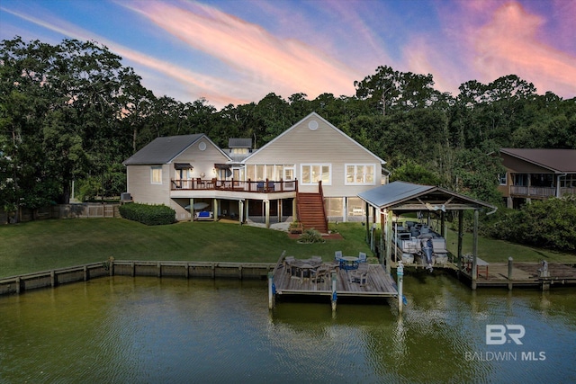 back of house with boat lift, a deck with water view, stairs, a lawn, and a carport