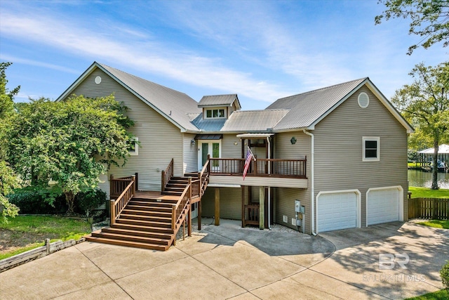 view of front of home featuring concrete driveway, an attached garage, a deck with water view, metal roof, and stairs