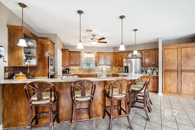 kitchen with brown cabinetry, light stone counters, a peninsula, stainless steel appliances, and a sink