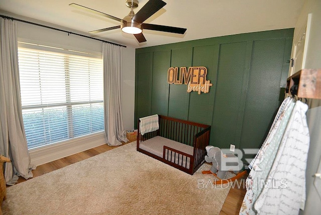 bedroom with a crib, ceiling fan, and light hardwood / wood-style floors