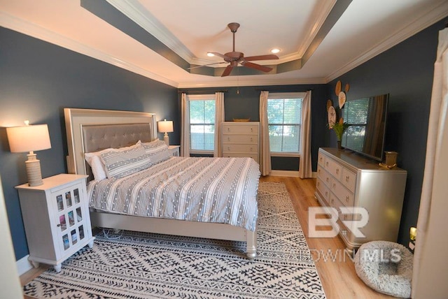 bedroom with ornamental molding, light hardwood / wood-style floors, ceiling fan, and a tray ceiling