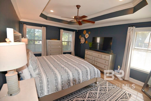 bedroom with wood-type flooring, ceiling fan, crown molding, and a tray ceiling