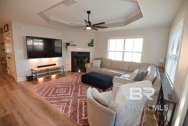 living room featuring ornamental molding, light wood-type flooring, ceiling fan, and a raised ceiling