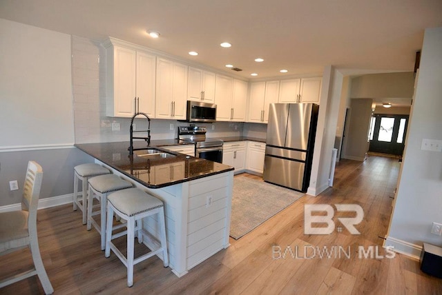 kitchen with kitchen peninsula, sink, white cabinetry, light wood-type flooring, and appliances with stainless steel finishes