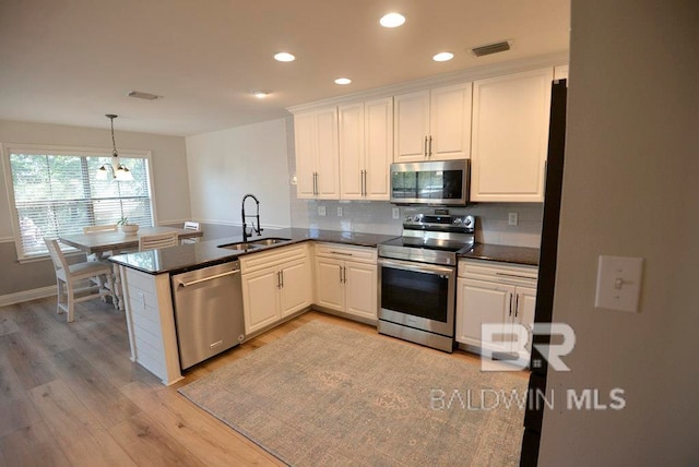 kitchen with white cabinets, kitchen peninsula, appliances with stainless steel finishes, and light wood-type flooring