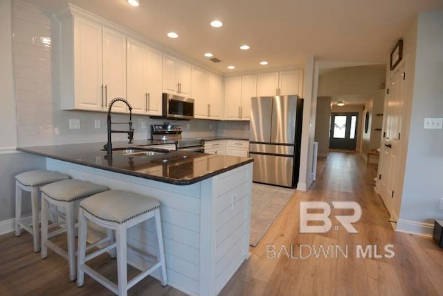 kitchen with white cabinetry, appliances with stainless steel finishes, sink, kitchen peninsula, and light hardwood / wood-style flooring