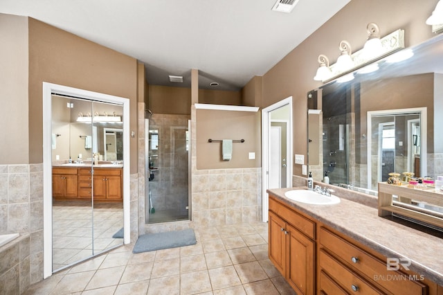 bathroom with tile walls, tile patterned floors, vanity, and plus walk in shower