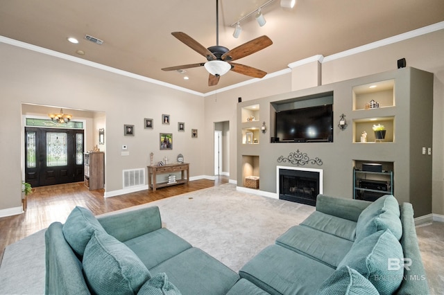 living room featuring rail lighting, hardwood / wood-style flooring, ornamental molding, ceiling fan with notable chandelier, and built in shelves